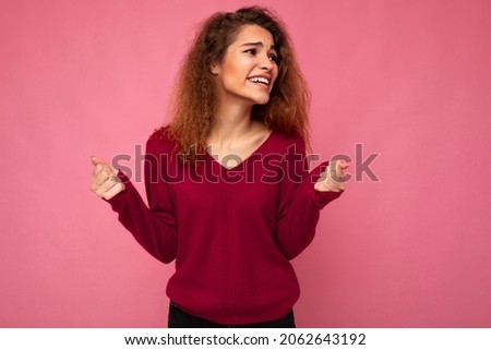 Photo of young emotional positive happy pretty brunette curly woman with sincere emotions wearing casual pink sweater isolated over pink background with copy space