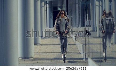 A young girl on an electric scooter rides on the sidewalk and enjoys a sunny day while rolling around a European city. Lifestyle. Environmentally friendly type of transport. Milan Italy Oct 2021 Royalty-Free Stock Photo #2062659611