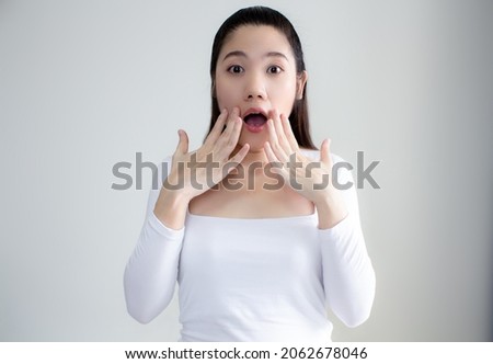 Asian women wear white t-shirt use hand touching her mouth with surprised and shocked on news, promotion,advertisment.
