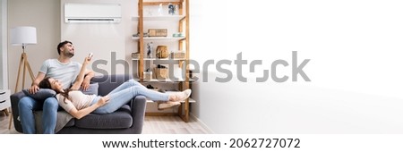 Happy Family Couple Using Air Conditioner. Apartment AC Royalty-Free Stock Photo #2062727072