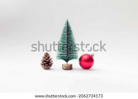 Brown pinecone with green and snow new year Christmas tree and red gift box stand next to each other on white pastel background. Copy space.