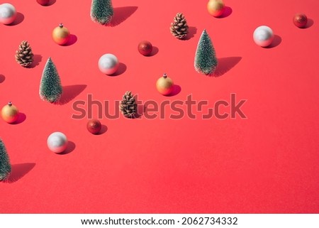 Arranged New Year and Christmas tree with yellow gold, silver, red  bauble and brown pinecone on a red pastel background. Pattern. Copy space.