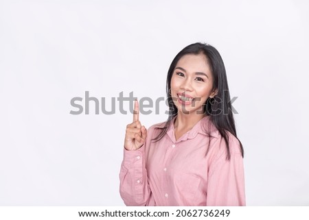 A pretty Filipina woman in a pink blouse points upward with her index finger. Copyspace on left. Isolated on a white background.
