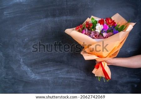 Beautiful bouquet in a man's hand on the background of a chalk board. Copy-space