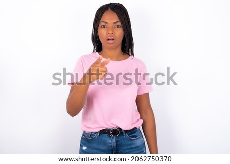 Shocked Young girl with dreadlocks wearing pink t-shirt on white backgrond points at you with stunned expression