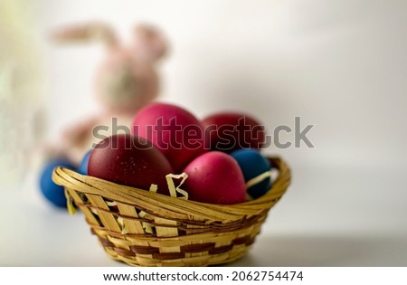 A basket of Easter eggs with a blurred image of a bunny in the background. Easter card concept.