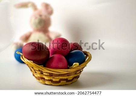 A basket of Easter eggs with a blurred image of a bunny in the background. Easter card concept.