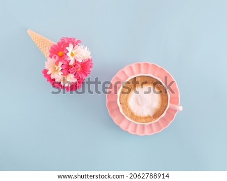 Romantic, vintage coffee cup with milk foam and spring floral bouquet in ice cream cone against pastel blue background. Creative composition, good morning theme. 
