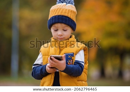 Happy child, playing with phone in the park, calling mommy, autumn pictures taken in the park, children playing