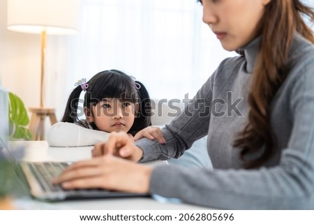 Asian young kid daughter feeling sad and need to play with busy mother. Attractive beautiful mom use laptop computer working from home during new normal and have no time for little child girl in house