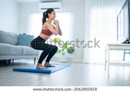 Asian Beautiful young woman stay home, doing aerobic exercise at home. Attractive girl doing lockdown activity, workout by squatting, follow instructions video from online trainer for health in house. Royalty-Free Stock Photo #2062805858