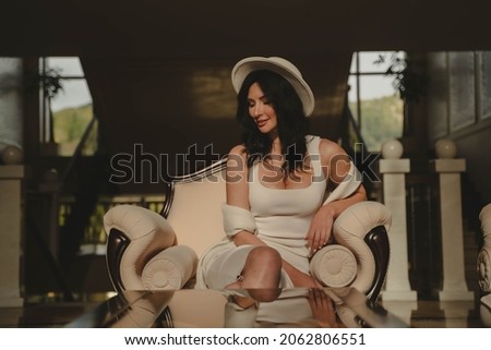 Beautiful girl in a white dress and hat sits in the lobby of an expensive hotel close up