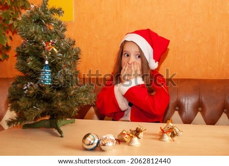 a little girl sitting at home in the kitchen looks away in surprise for the New Year and Christmas 2022