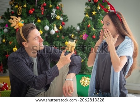 In the concept picture, Christmas gifts. Young Caucasian man giving a gift in a golden box to a young woman or lover. Woman is excited and shocked when she receives a gift.