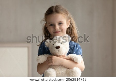 Portrait of smiling adorable preschool small kid girl cuddling favorite fluffy toy, posing alone at home. Happy cute 7s little child daughter holding teddy bear, feeling cheerful in kindergarten.