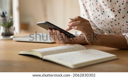 Hands of freelance woman making notes on smartphone and in notebook, planning work calls. Student preparing for exam, using learning app on mobile phone, writing in copybook. Close up, cropped shot Royalty-Free Stock Photo #2062830302