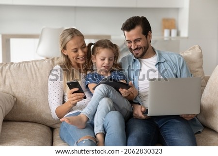 Happy bonding loving family couple parents with little preschool kid daughter holding different modern technology gadgets, spending time online sitting on comfortable couch addiction concept. Royalty-Free Stock Photo #2062830323