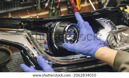 Car headlight in repair close-up. An auto mechanic wearing gloves installs the lens into the headlight housing. The concept of a car service.Installation of LED lenses in the headlight. LED lenses. Royalty-Free Stock Photo #2062834010