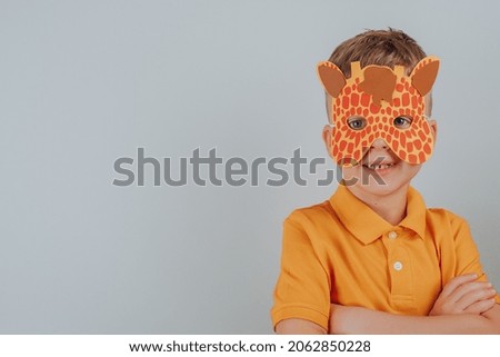 Smiling child with carnival giraffe mask isolated on gray background. School, kindergarten. Children's hands cut, glue, make. space for text. High quality photo
