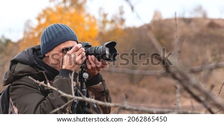 Front view of young male photographer taking pictures in autumn forest
