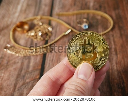 hand takes the golden bitcoin near  golden jewelry on wooden background, pawn shop concept, closeup