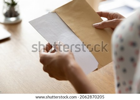 Hands of woman receiving letter, invitation, notification, postcard, taking out document for reading, opening envelope with blank folded paper at work desk. Mail concept. Close up, cropped shot Royalty-Free Stock Photo #2062870205