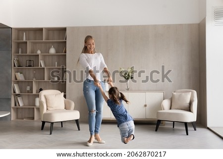Full length happy beautiful young woman twisting in air cheerful small preschool child daughter, involved in carefree entertaining family activity together in modern living room, carefree pastime. Royalty-Free Stock Photo #2062870217