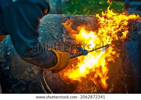 The texture of hot metal from acetylene welding. Welder's hands in protective gloves during operation. Cutting a metal pipe outside during the day. Royalty-Free Stock Photo #2062872341
