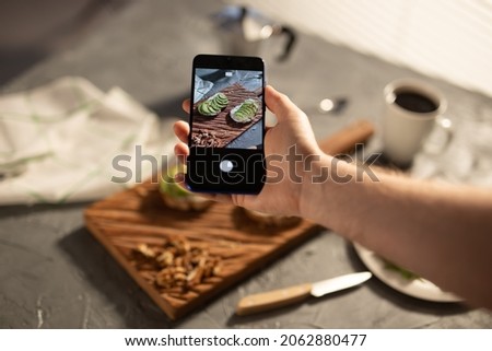 Hands take pictures on smartphone of two beautiful healthy sour cream and avocado sandwiches lying on board on the table. Social media and food concept