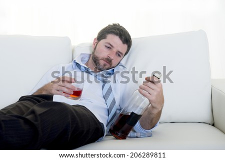 caucasian businessman alcoholic wearing a blue work shirt and tie drunk and drinking  Scotch or Whiskey sitting on a sofa at home after a long day or week of work on a white background. 