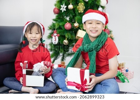 Asian siblings opening presents next to  tree at home to celebrate Christmas Day