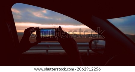 silhouette of  man traveler sitting  inside car, looking and taking  pictures on a smartphone.  beautiful sunset in mountains. take a photo. 