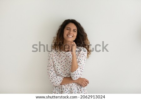 Happy pretty Hispanic young 30s woman in casual looking at camera with toothy smile, laughing, touching facial skin. Studio portrait of female model isolated on white background. Head shot.