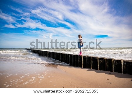Young girl standing on the wooden bridge in the ocean by the beach in the Poland.