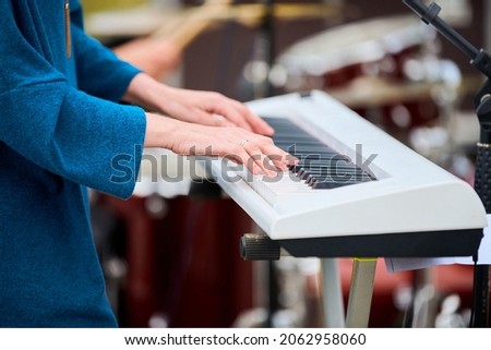 Musician woman playing on white synthesizer keyboard piano keys, focus on female hands on synthesizer. Musician playing musical instrument on concert stage, cropped image of person playing synthesizer Royalty-Free Stock Photo #2062958060