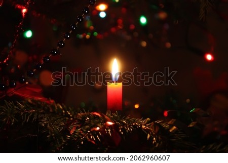 Burning candle in candlestick on decorated Christmas tree branch.