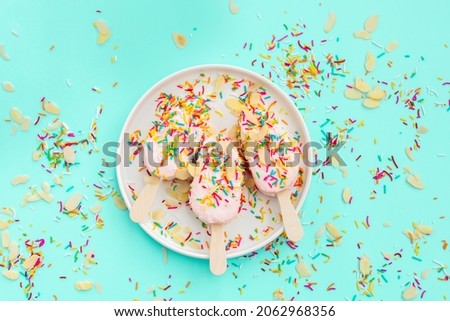 Bright and colorful flat lay of pink strawberry Popsicle ice cream on blue background. Healthy summer food concept. Top view of popsicle with sprinkles, overhead
