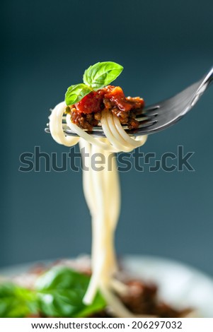 Fork full of twirled Italian spaghetti with a Bolognese meat sauce and basil suspended in the air above a full plate of food against a grey background
