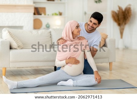 Loving muslim husband rubbing his pregnant wife shoulders, expecting arab family enjoying healthy lifestyle during pregnancy, doing sport at home in living room