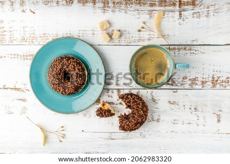 Sweet glazed chocolate donut on vintage turquoise plate and hot coffee cup on rustic wooden background. Top view pastry good morning card with copy space