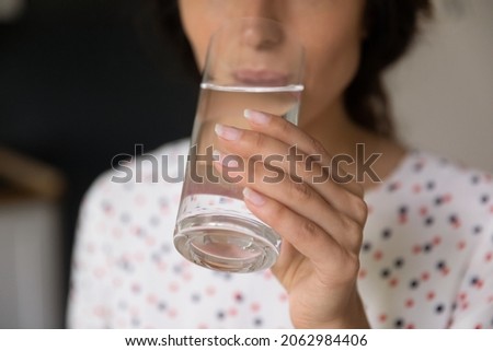 Hand of woman holding glass and drinking fresh pure still cold water, satisfying thirst, keeping detox, healthy hydration and diet, losing weight. Wellness, healthcare, refreshment concept. Close up Royalty-Free Stock Photo #2062984406