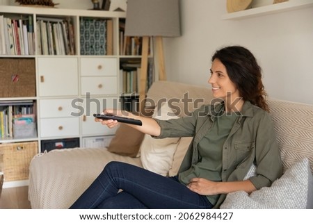 Happy homeowner resting on couch, watching movie on TV. Sport football fan relaxing at home, holding remote control, turning on football soccer game on sport channel. Digital television concept