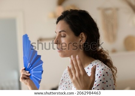 Exhausted overheated sweaty woman suffering from heat at home without conditioner, trying to cool too hot air with handheld fan in summer day, feeling unwell du to weather, humidity, air temperature Royalty-Free Stock Photo #2062984463
