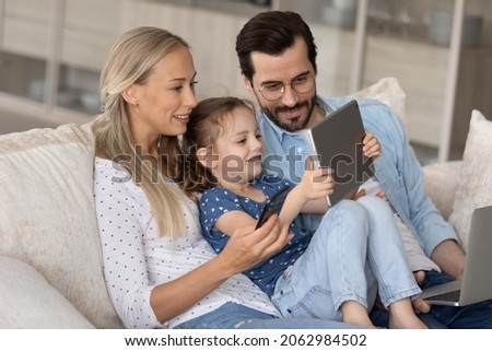 Addicted to modern technology happy young family couple with adorable little preschool child daughter using different gadgets, playing mobile games online or watching cartoons, spending time online.
