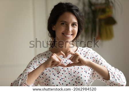 Happy thankful Hispanic woman making finger heart shaped hand gesture, showing love sign, expressing, support, gratitude, solidarity, promoting donation charity campaign. Head shot portrait Royalty-Free Stock Photo #2062984520