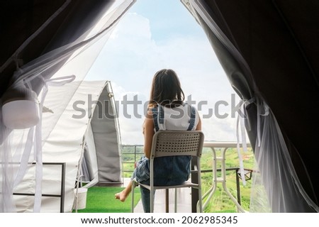 Back view of asian woman sitting on front a tent among the mountain in countryside on vacation