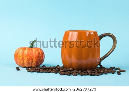 Orange coffee mug, coffee beans and a small pumpkin on a blue background. Pumpkin style.