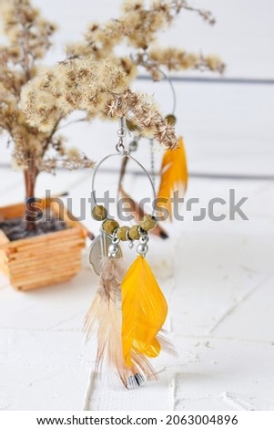 beautiful earrings rings with yellow feathers on a branch of dried flowers