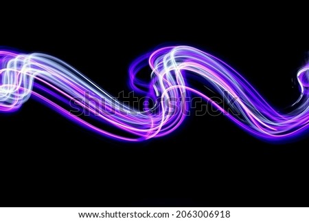 Long exposure light painting photography. Abstract pink purple swirls in a parallel lines pattern against a black background.