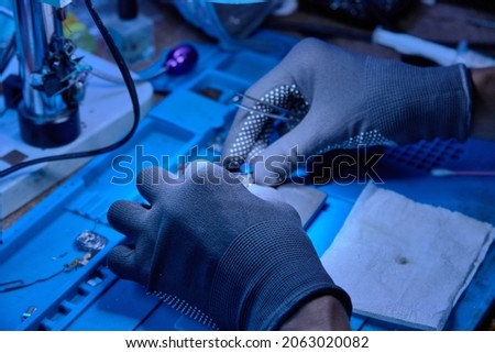 The hands in gloves of cellphone technology device maintenance engineer (professional repairman) work on the smartphone . Close-up macro photo, selective focus